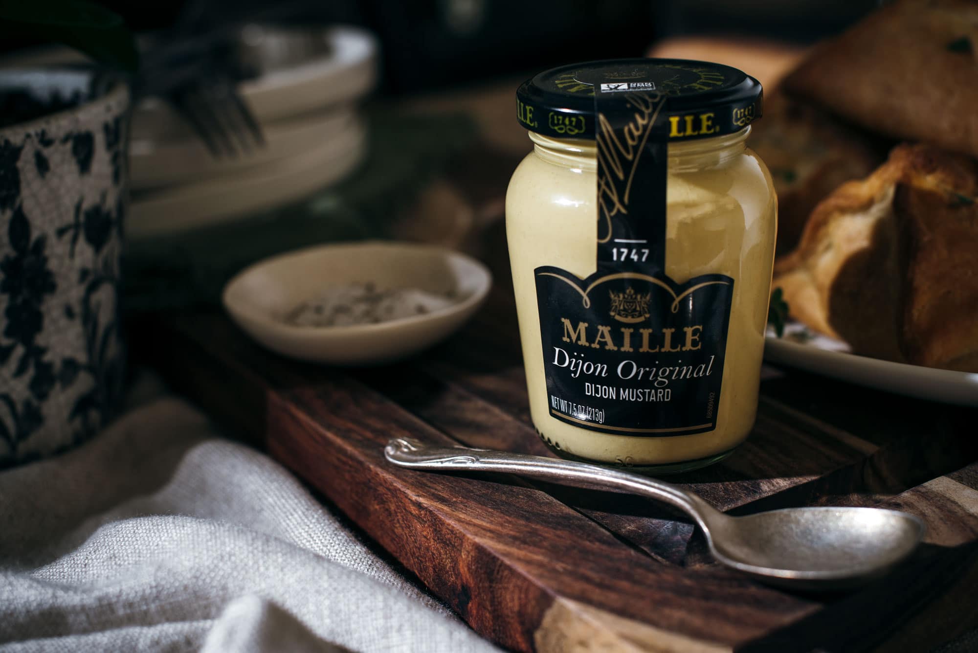 Jar of Maille Dijon Originale Mustard with serving spoon on wooden board
