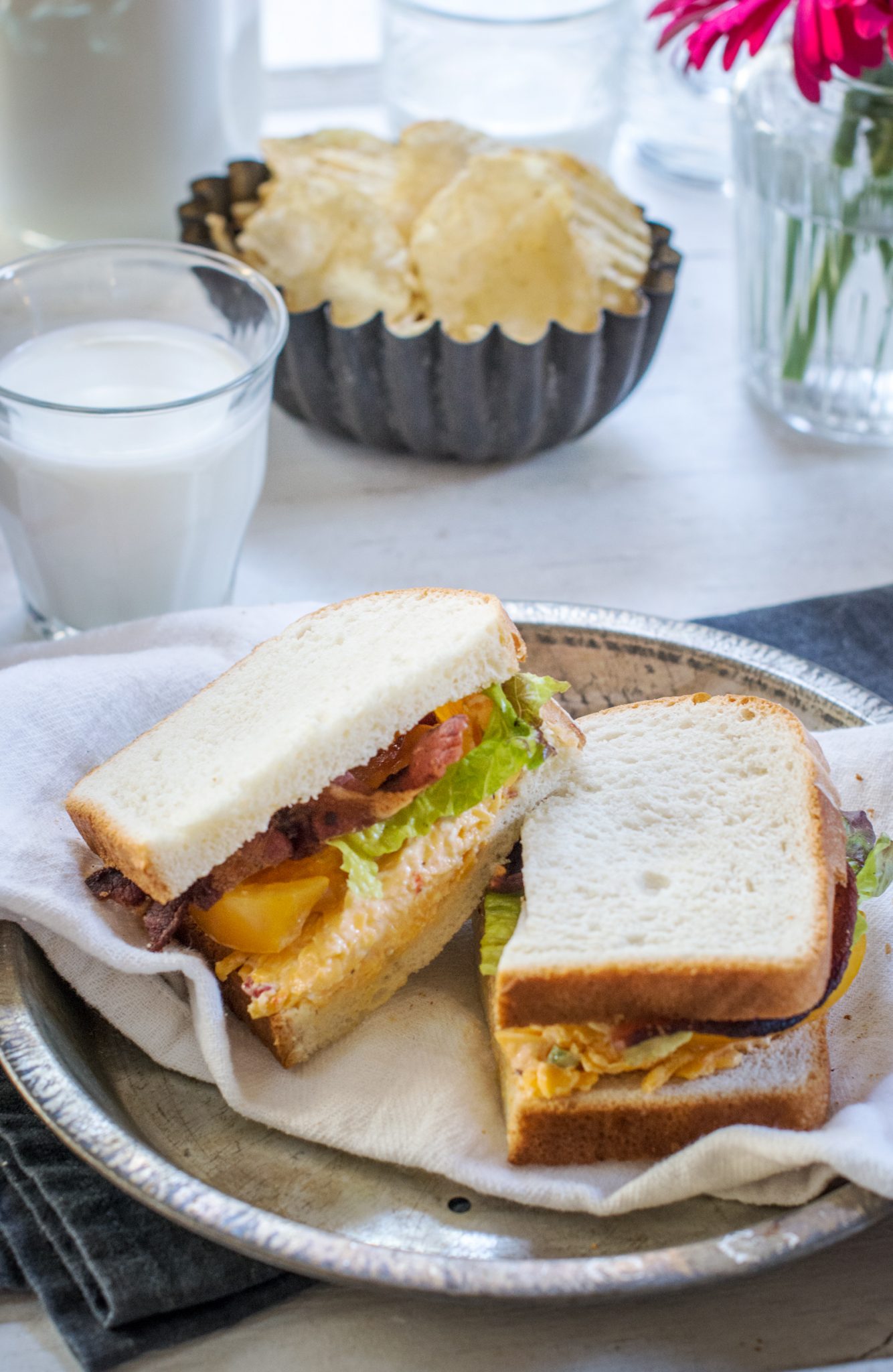 Glass of milk, bowl of potato chips and a sliced BLT sandwich on Pepperidge Farm hearty white bread.