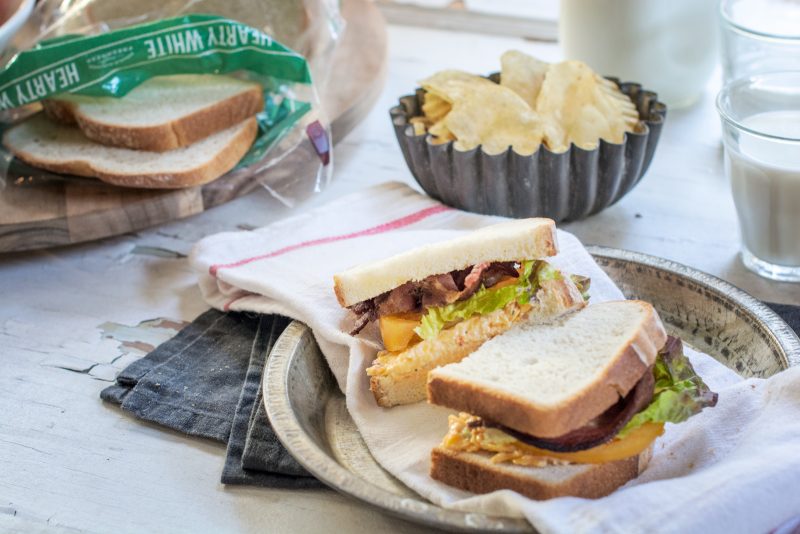 A sliced BLT sandwich with potato chips on the side and opened bag of Pepperidge Farm hearty white bread