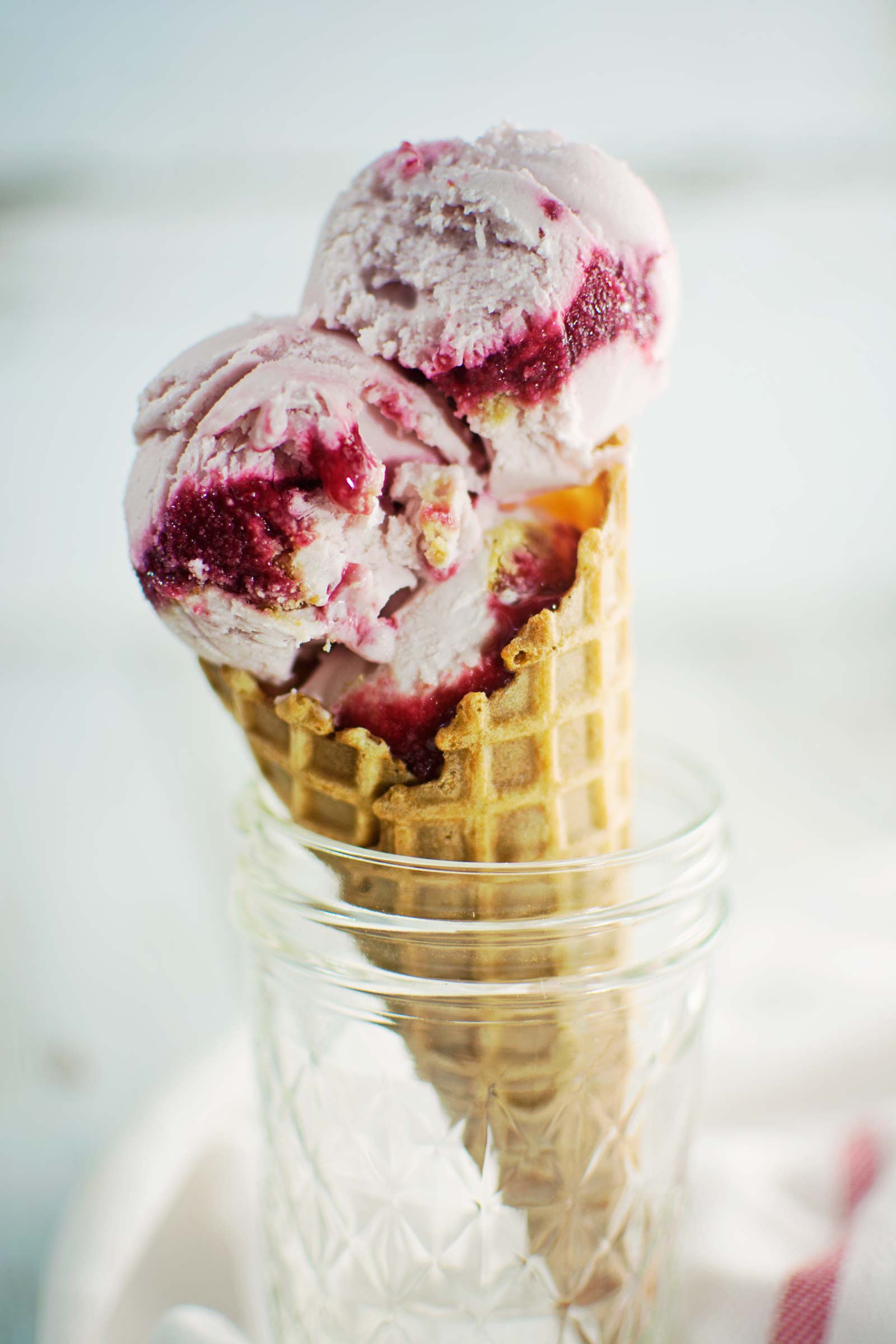 Two scoops of swirled raspberry cheesecake ice cream in a waffle cone that's sitting in a jar