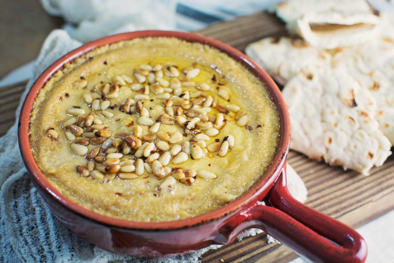 Try this Baked Hummus topped off with buttery, toasted pine nuts and served up with some pita bread! It's great for your next get together, or as a snack. Recipe @LittleFiggyFood