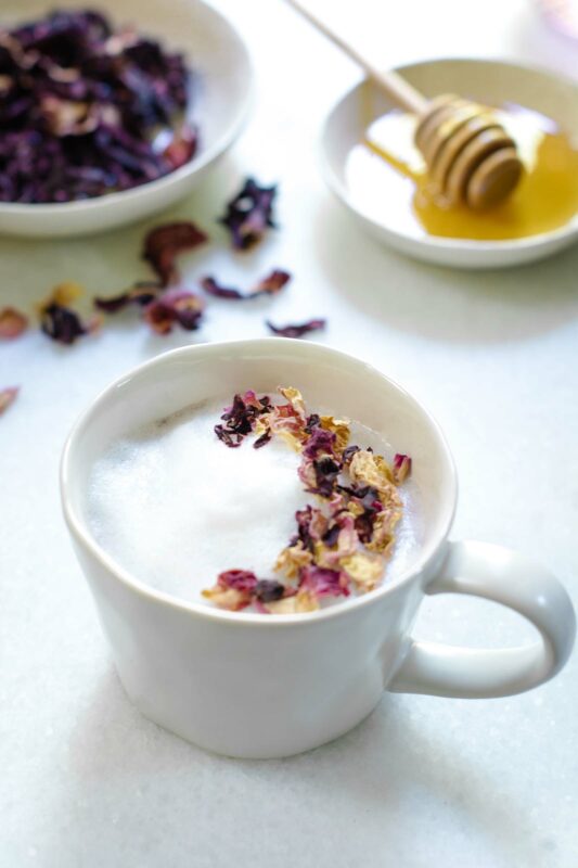 White mug of Hibiscus Flower tea and steamed milk decorated with pink flowers