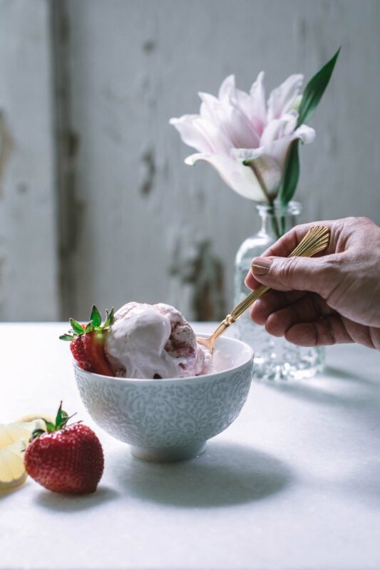 White table with bowl of pink yogurt and hand holding gold spoon