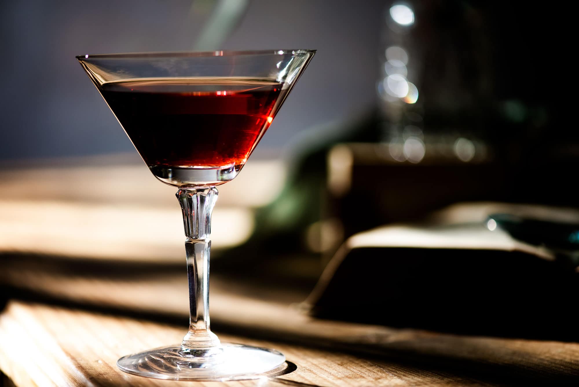 Martini glass with red drink sitting on a wood counter